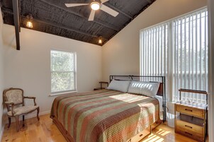 A bedroom with a bed, a chair, a bedside table, a window with blinds, and a ceiling fan.