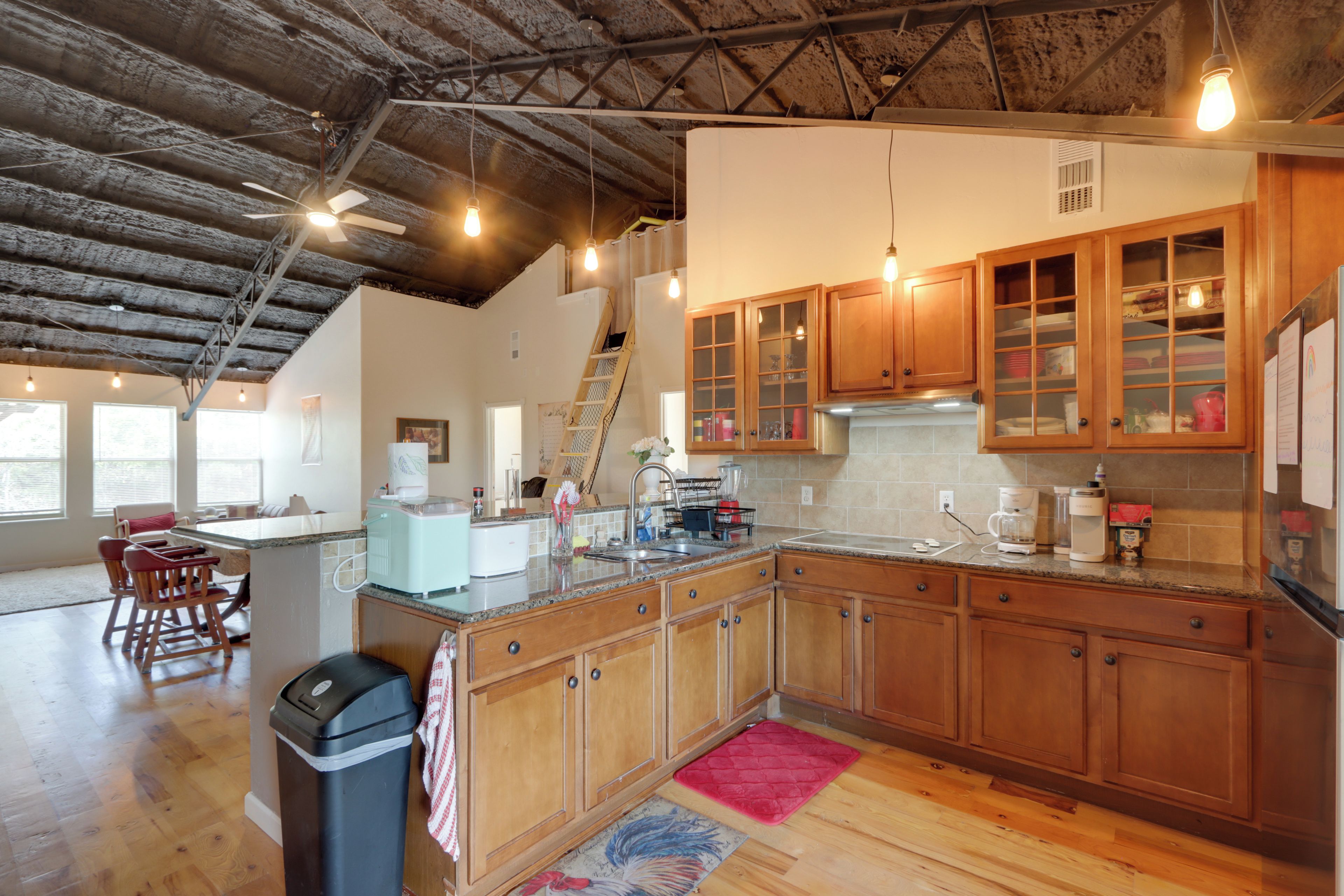 A spacious kitchen with wooden cabinets, a granite countertop, and a view of the living area.