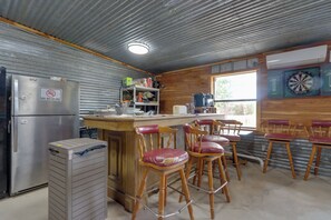 A kitchen with a stainless steel refrigerator, wooden bar stools, and a dartboard on the wall.