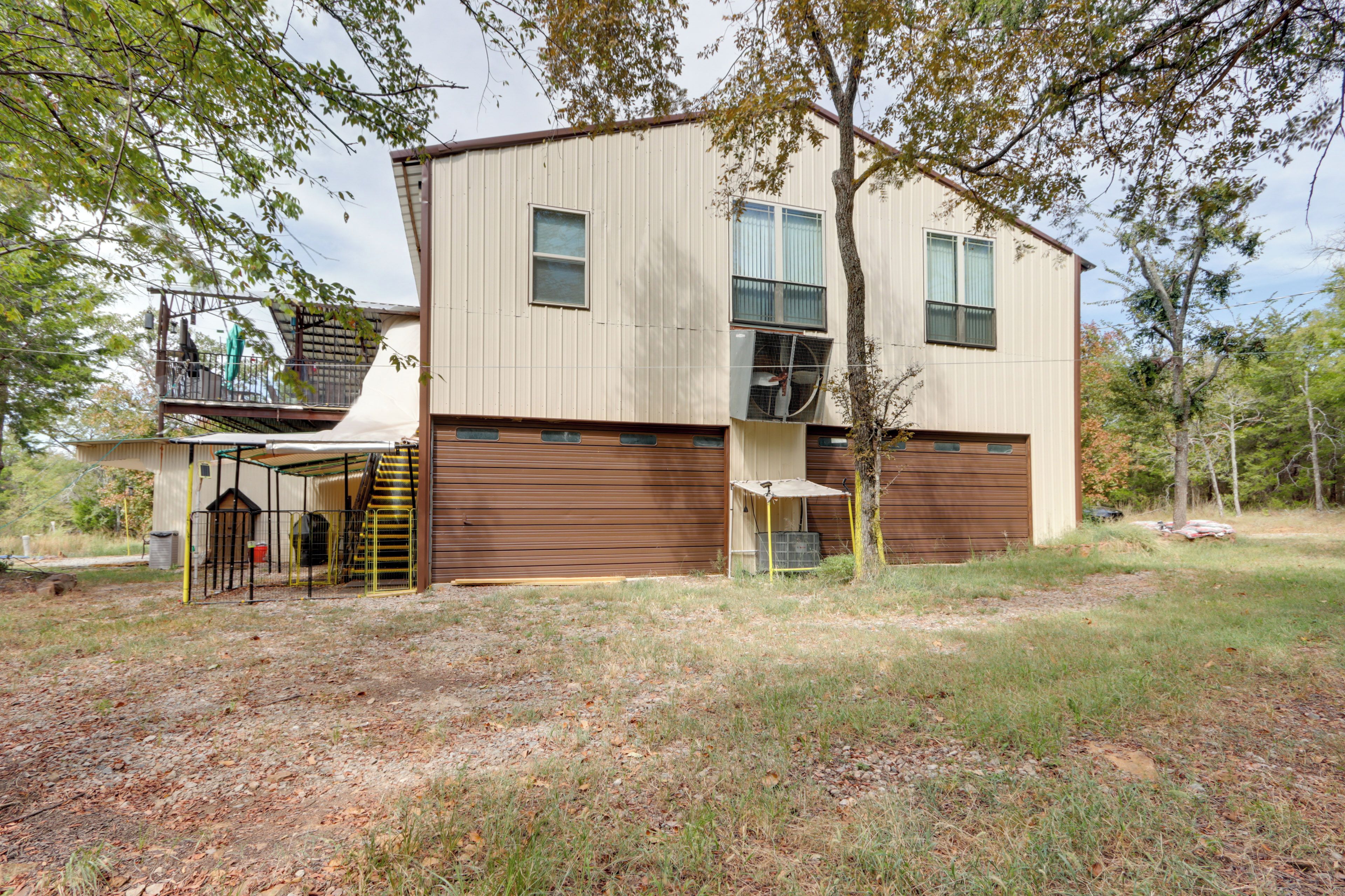 A two-story building with a garage door, a covered outdoor area, and a tree in front.