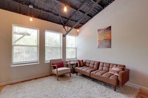Una habitación con un sofá de cuero marrón, una silla de madera, un tapete blanco y dos ventanas con persianas.