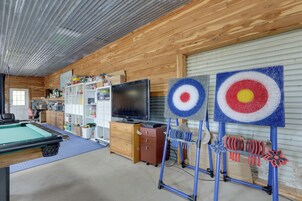 A recreational room with a pool table, shelves with various items, a television, and two target boards.
