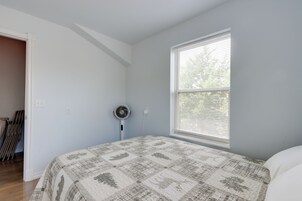 Un dormitorio con cama, ventilador, ventana con persianas y puerta que da a otra habitación.