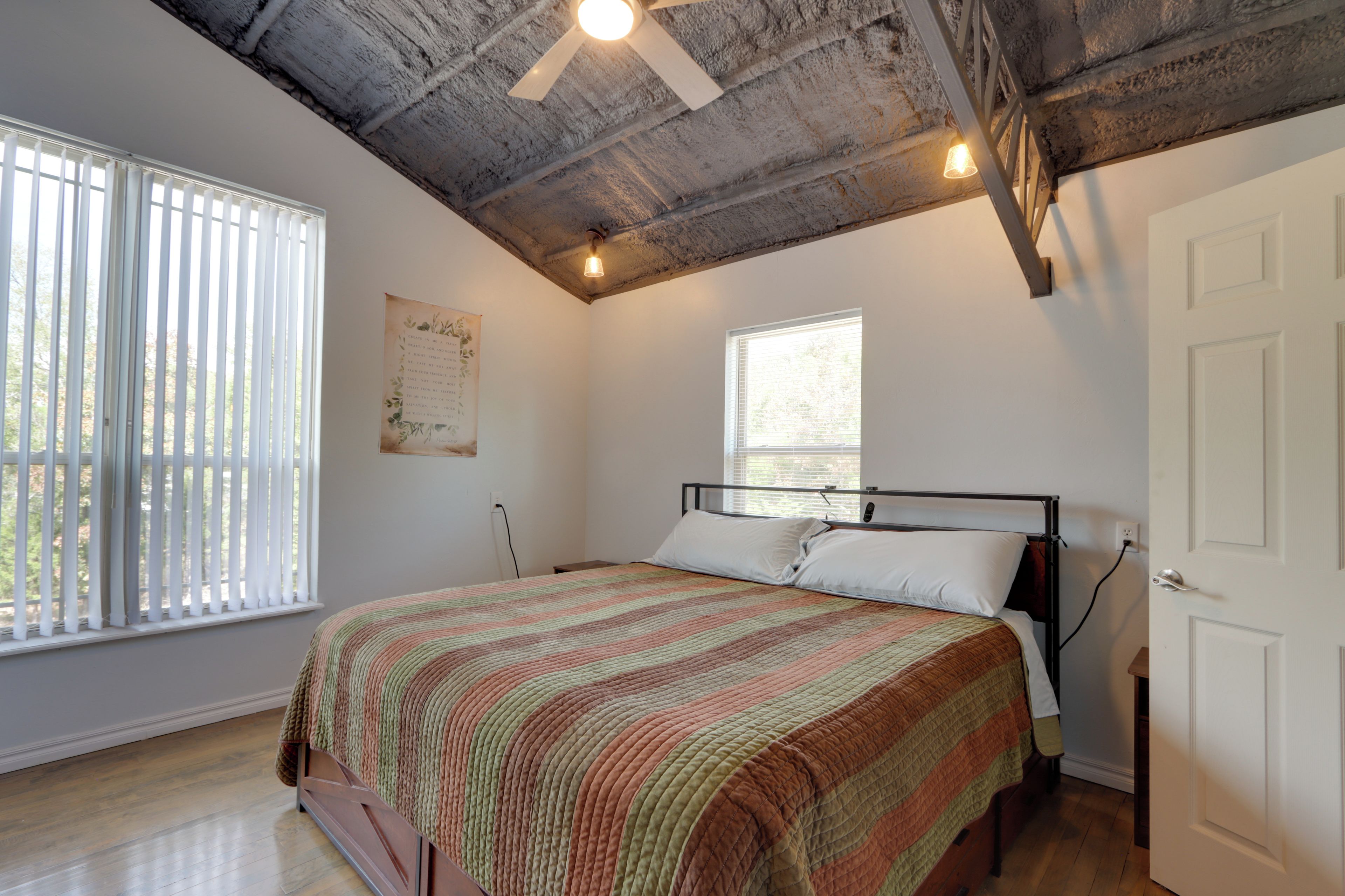 A bedroom with a bed, a ceiling fan, a window, and a door.