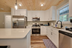 A modern kitchen with stainless steel appliances, white cabinetry, and a wooden ceiling. - Home Near Kentucky Lake & Paris Landing! (Buchanan)