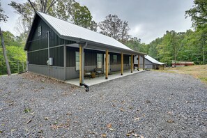 A modern building with a sloped metal roof, a covered porch with chairs, and a gravel driveway. - Home Near Kentucky Lake & Paris Landing! (Buchanan)