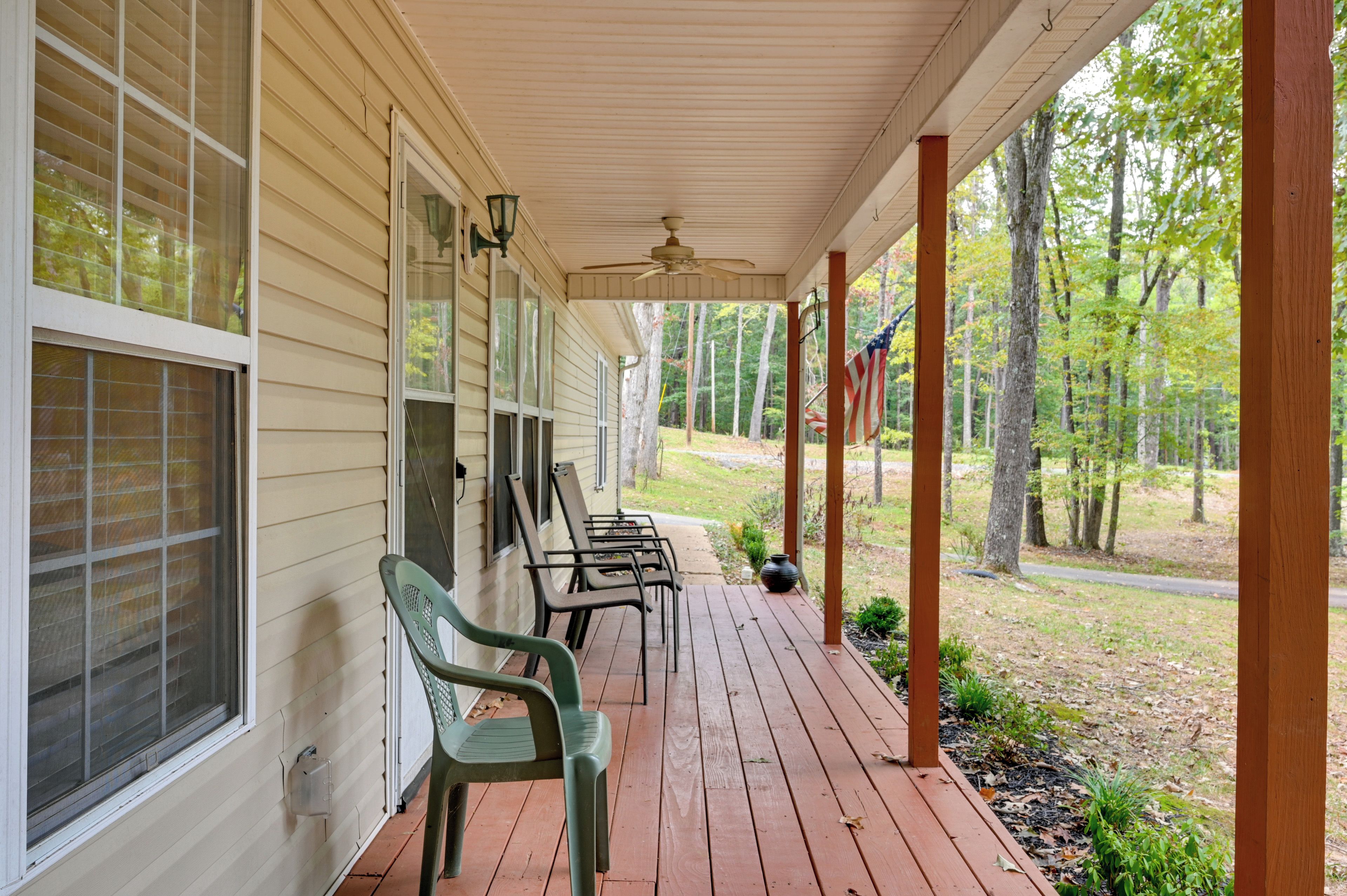 A covered porch with wooden flooring, a ceiling fan, and a row of chairs.