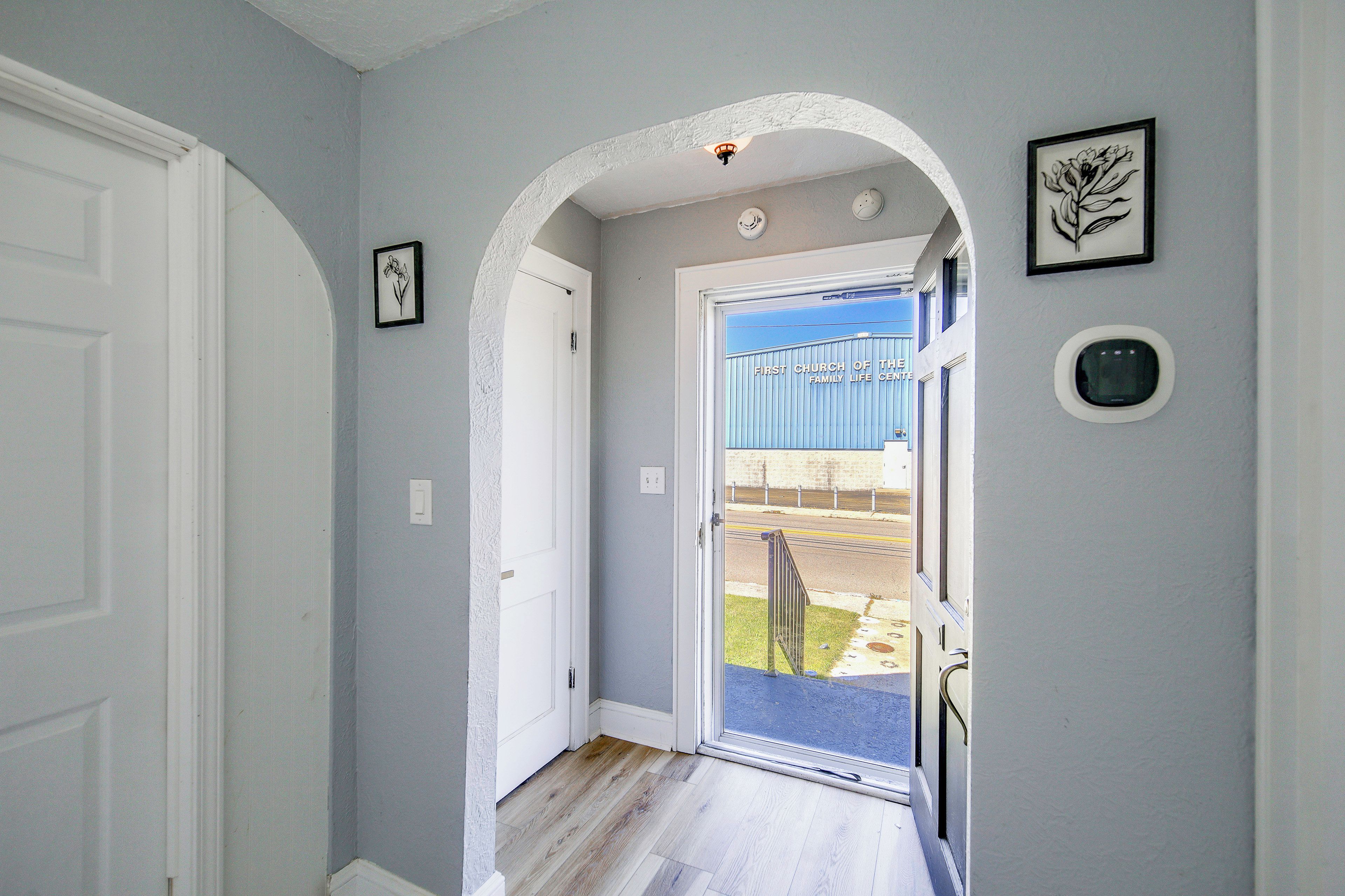 A hallway with a white door, a framed picture, and a view of a building with a sign reading 'First Church of the Family Life Center'.
