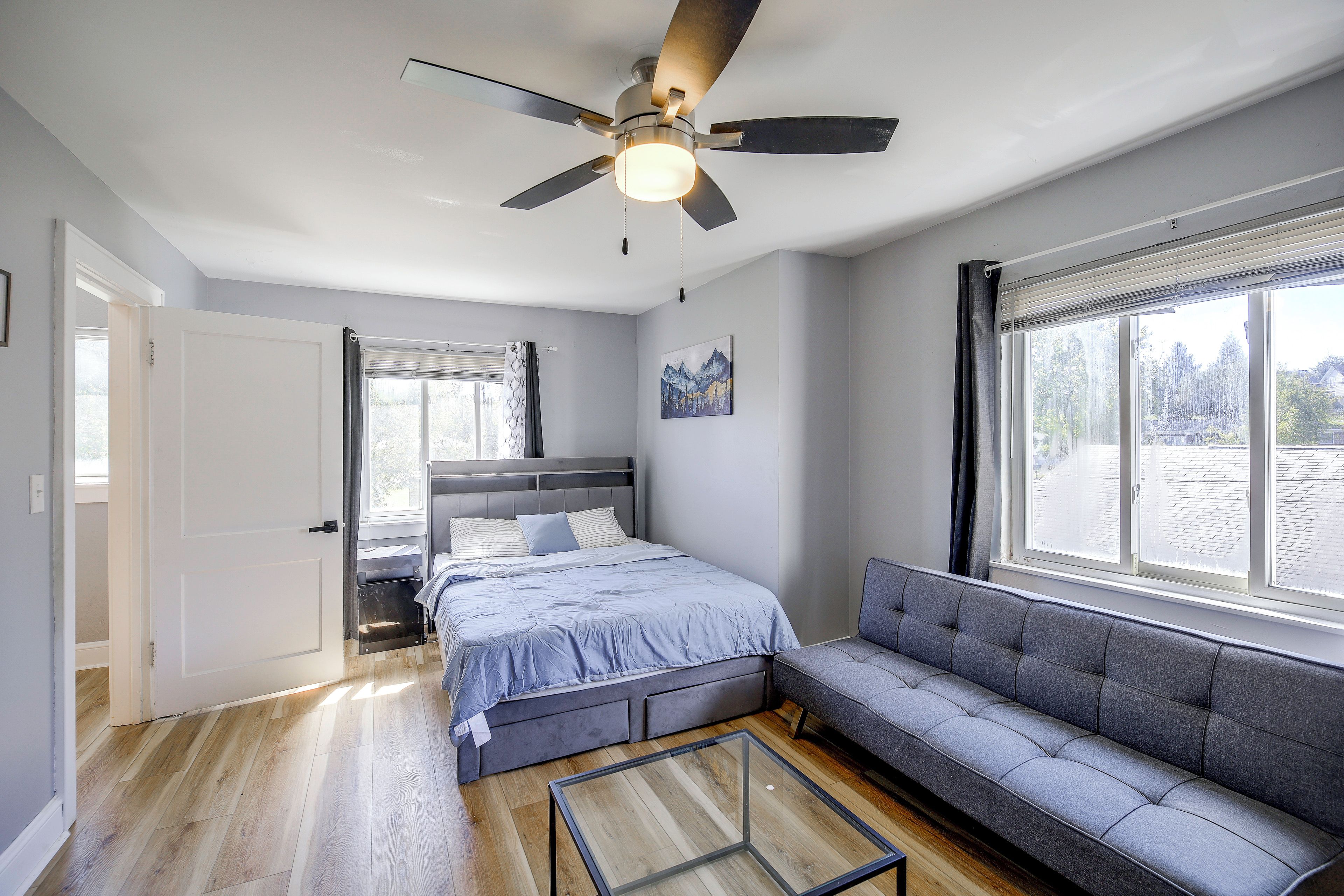 A bedroom with a bed, a sofa, a ceiling fan, and a window.