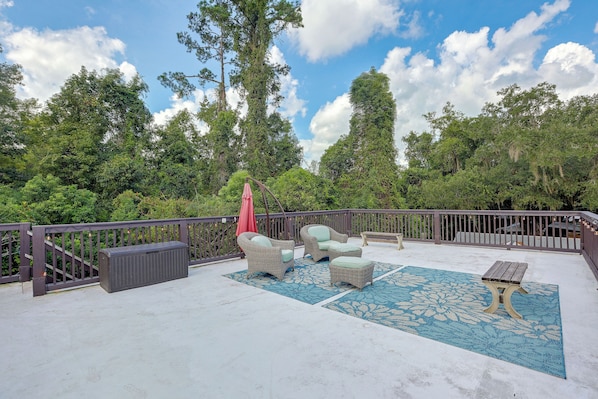 A covered outdoor patio with wicker furniture, a red umbrella, and a blue patterned rug.