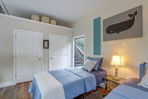 A bedroom with two beds, a window with a view of trees, and a whale artwork on the wall.