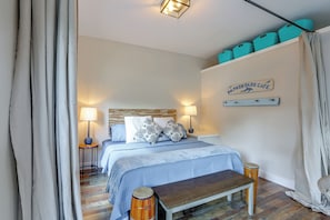 A bedroom with a bed, bedside lamps, a bench, a wooden headboard, a wall-mounted shelf with storage bins, and a sign reading 'Dolphin Park Cafe'.