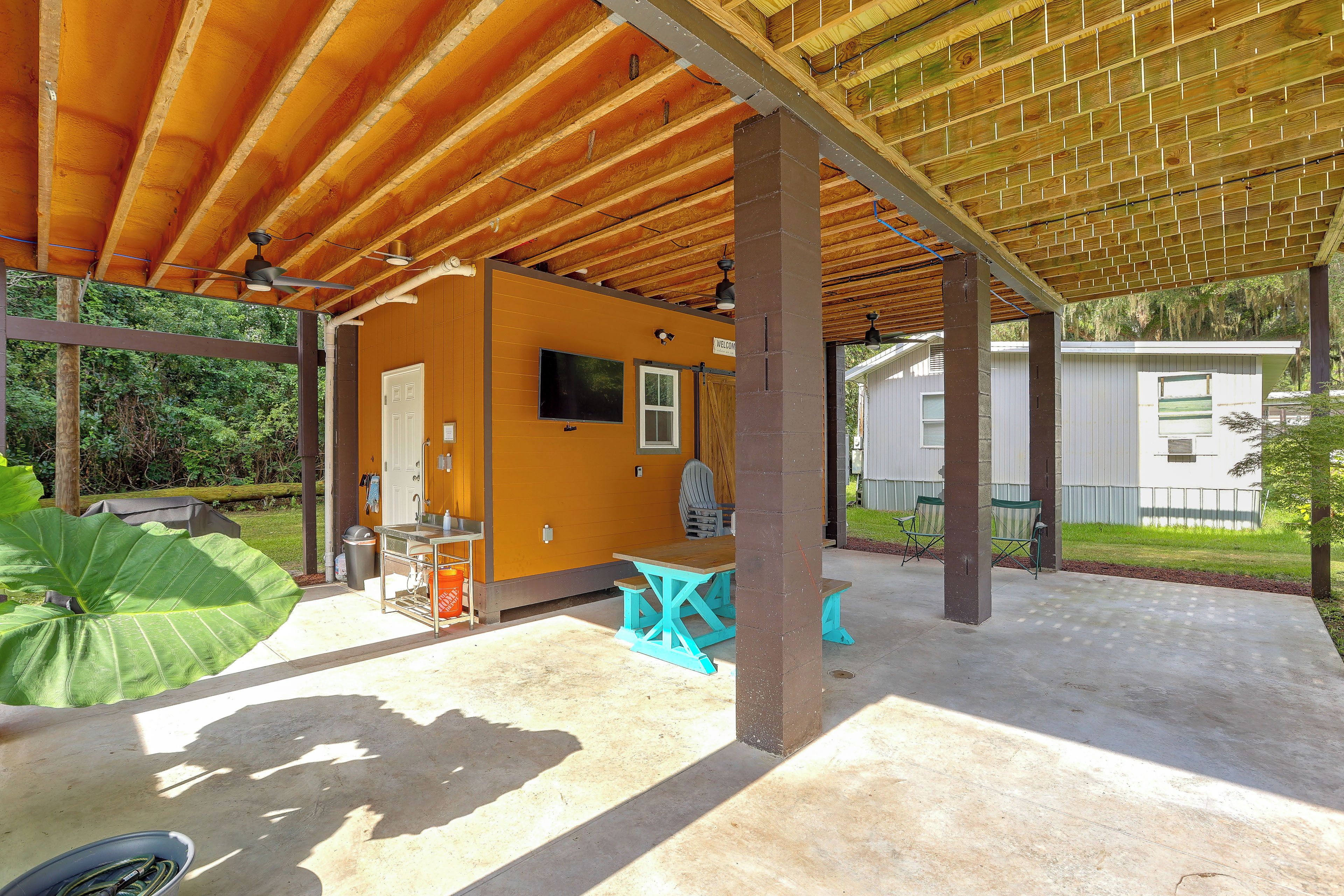 A covered outdoor area with a wooden ceiling, a small building with a TV, and outdoor seating.