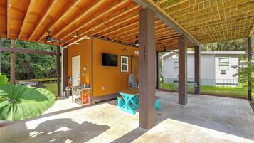 A covered outdoor area with a wooden ceiling, a small building with a TV, and outdoor seating.