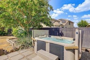A hot tub with a stone exterior, surrounded by a wooden fence, and a house with solar panels in the background. - Hot Tub & Patio! Family Escape, 7 Mi to Seaworld (San Antonio)