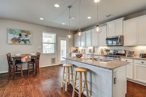 A modern kitchen with white cabinets, a granite countertop, a built-in microwave, and a stainless steel stove. There are two wooden stools at the island, and a painting hangs on the wall. - Hot Tub & Patio! Family Escape, 7 Mi to Seaworld (San Antonio)