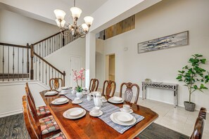 A dining area with a wooden table set for four, chairs, a chandelier, a staircase, and a painting on the wall. - Home Theater & Game Room! 7BR San Antonio Retreat (San Antonio)