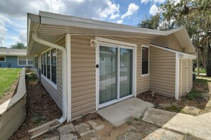 A single-story house with a covered porch, a sliding glass door, and a small front yard with mulch and a concrete path. - The Wandering Parrot: Pool, Pickleball & Lake (Clermont)