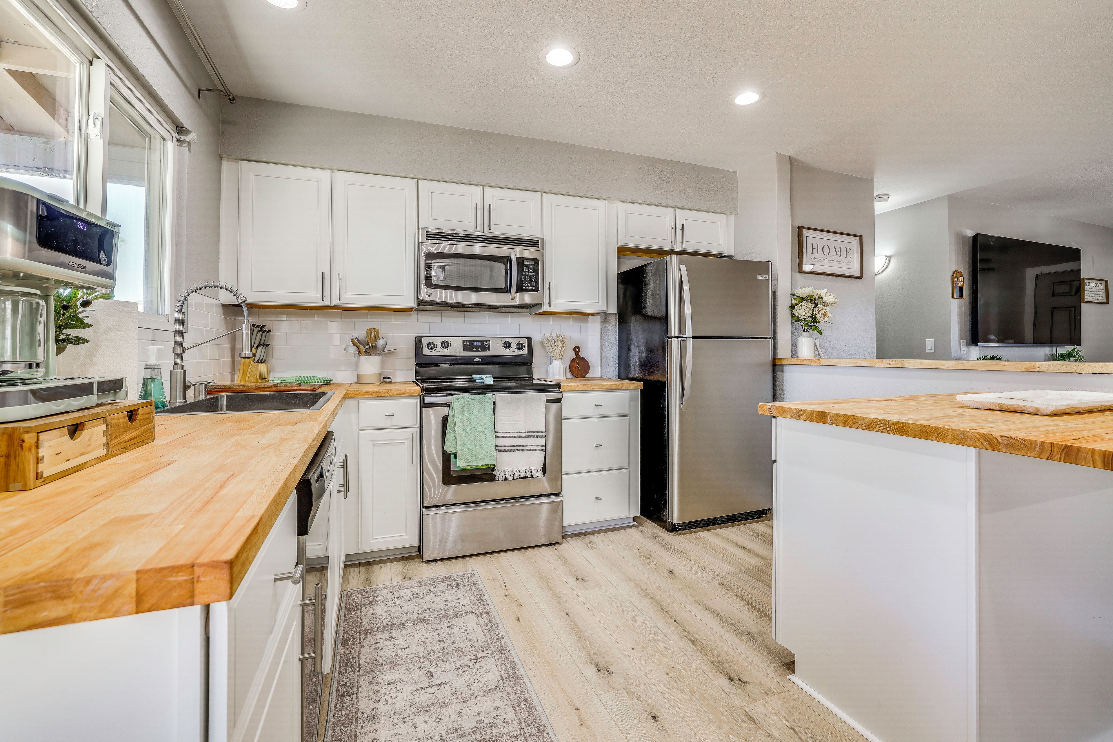 A modern kitchen with white cabinets, stainless steel appliances, and wooden countertops.