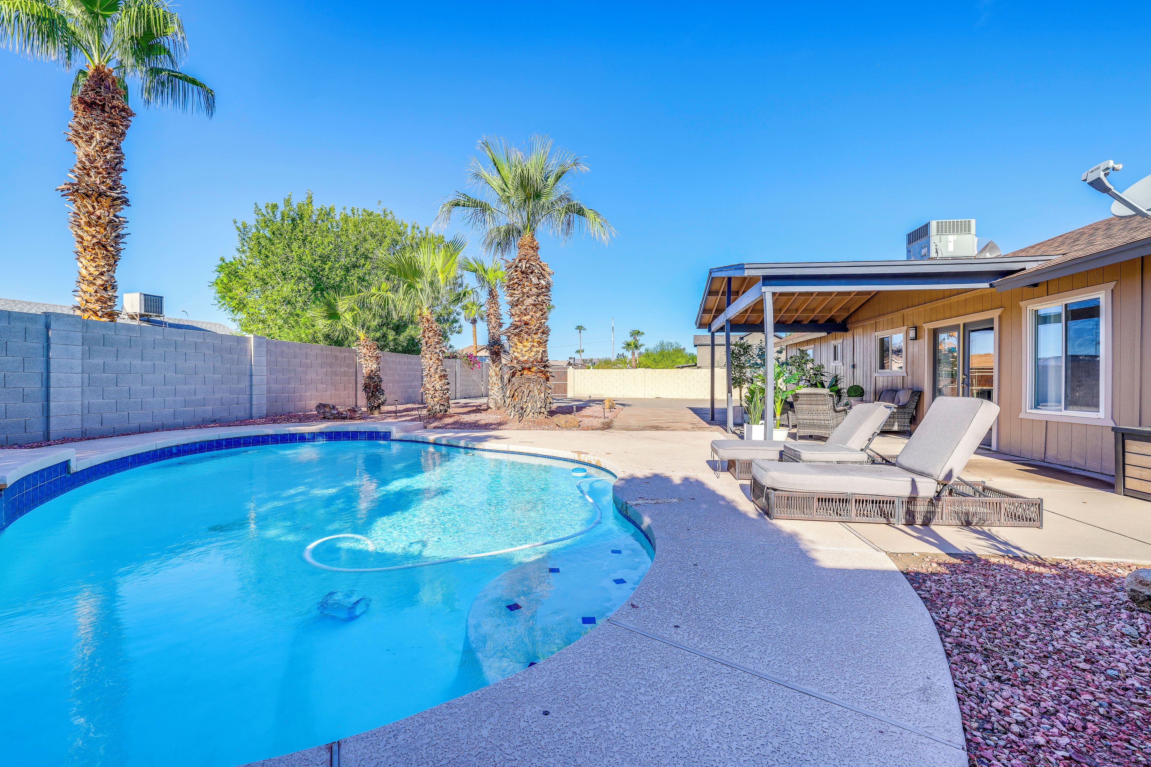 A swimming pool with a curved edge, surrounded by a stone deck and palm trees.