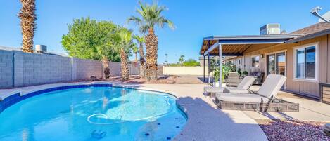 A swimming pool with a curved edge, surrounded by a stone deck and palm trees.