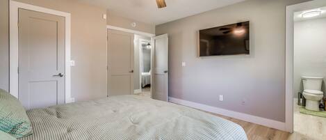 Un dormitorio con cama, ventilador de techo, televisión y baño con inodoro y lavamanos.