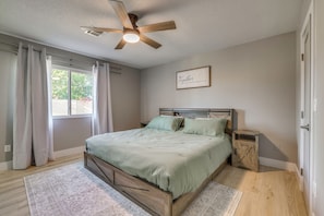 A bedroom with a bed, a nightstand, a ceiling fan, a window with curtains, and a motivational quote on the wall. - Chandler Haven Near Golf, Sports & Shopping! (Chandler)