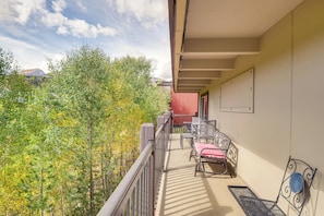 A balcony with outdoor furniture, a view of trees, and a building in the background. - Breckenridge Ski Condo: Easy Bus to Slopes (Breckenridge)