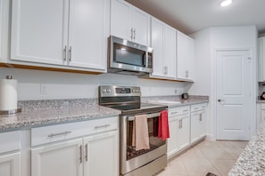A kitchen with white cabinets, a stainless steel microwave, an oven, and a granite countertop. - Port St. Lucie Home on Florida's Treasure Coast (Port Saint Lucie)