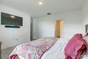 Ein Schlafzimmer mit einem Bett, einem flachbildfernseher an der Wand und einer Tür zu einem weiteren Raum.