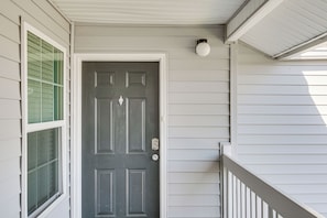 A front door with a window to the left, a porch with a railing, and a ceiling with a light fixture. - 5 Mi to Beach! Gulf Shores Condo w/ Pool & Hot Tub (Gulf Shores)