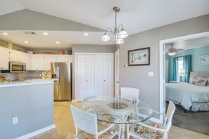 A modern kitchen with white cabinets, stainless steel appliances, and a dining area with a glass table and wicker chairs. - 5 Mi to Beach! Gulf Shores Condo w/ Pool & Hot Tub (Gulf Shores)