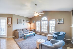 A living room with a ceiling fan, a sofa, a coffee table, and a blue armchair. - 5 Mi to Beach! Gulf Shores Condo w/ Pool & Hot Tub (Gulf Shores)