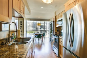 A modern kitchen with stainless steel appliances, a granite countertop, and a view of buildings through large windows. - Beach + Poolside Days! Extended Coronado Escape (Coronado)