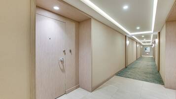 Corredor de hotel com piso carpete, portas de madeira e iluminação embutida.
