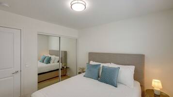 A bedroom with a bed, a bedside table with a lamp, a mirror, and a door.