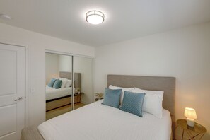 A bedroom with a bed, a bedside table with a lamp, a mirror, and a door. - Coachella Getaway w/ Yard! Near Festivals & Golf (Coachella)