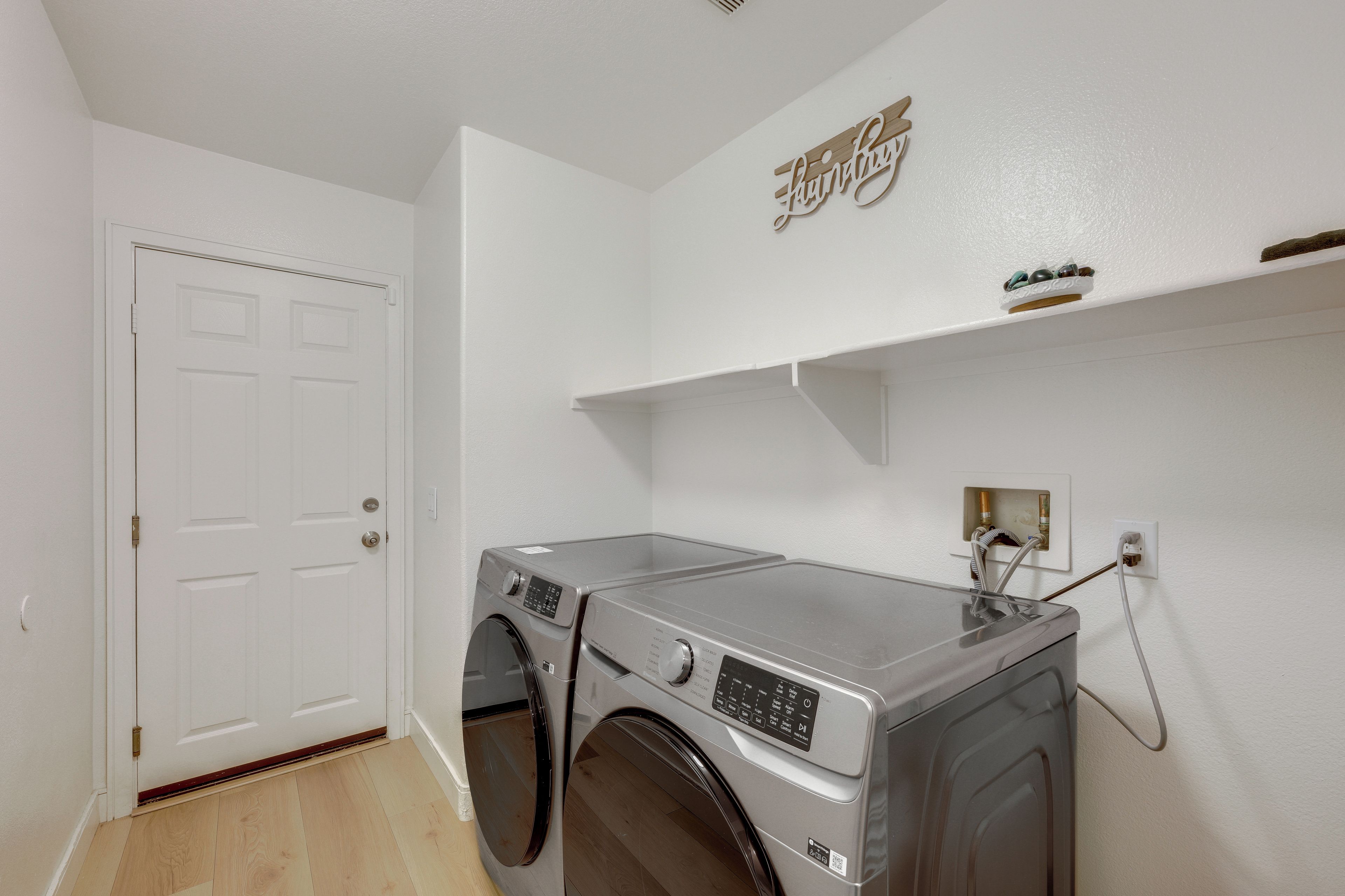A laundry room with a front-loading washing machine, a dryer, and a wall-mounted shelf above the dryer.