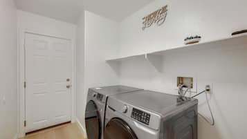 A laundry room with a front-loading washing machine, a dryer, and a wall-mounted shelf above the dryer.