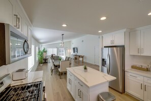 A modern kitchen with a central island, stainless steel appliances, and a dining area with a table and chairs. - Coachella Getaway w/ Yard! Near Festivals & Golf (Coachella)