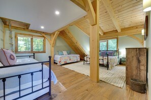 Une chambre spacieuse située dans les combles, avec deux lits, des poutres apparentes et de grandes fenêtres.