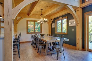 A dining area with a wooden table and chairs, large windows, and a hanging light fixture.
