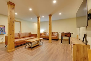 Ein Zimmer mit Holzsäulen, zwei Sofas, einem Couchtisch, einem Kicker und einem flachbildfernseher an der Wand.
