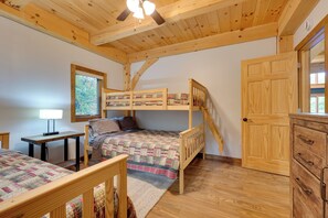 A room with two bunk beds, a desk, a dresser, and a window with a view of trees.