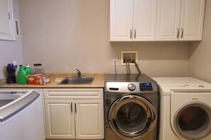 Un espace buanderie comprenant un lave-linge, un sèche-linge et un évier.