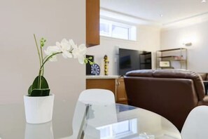 Un salon moderne avec une table en verre, des chaises blanches, un canapé en cuir marron et une orchidée blanche dans un vase.