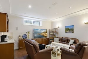 A living room with a brown leather sofa, a television, and a dining table with chairs.