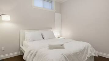 A bedroom with a bed, a nightstand, a lamp, and a window.
