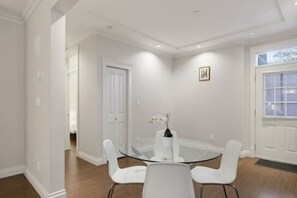 Un comedor con mesa de vidrio y sillas blancas, una puerta blanca y un ventanal con vistas.