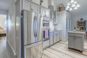 A modern kitchen with stainless steel appliances, a herringbone tile backsplash, and a floating island with a wine bottle and glasses. - Comfortable Cabin w/ Hot Tub, Near Old Midtown (Ruidoso)